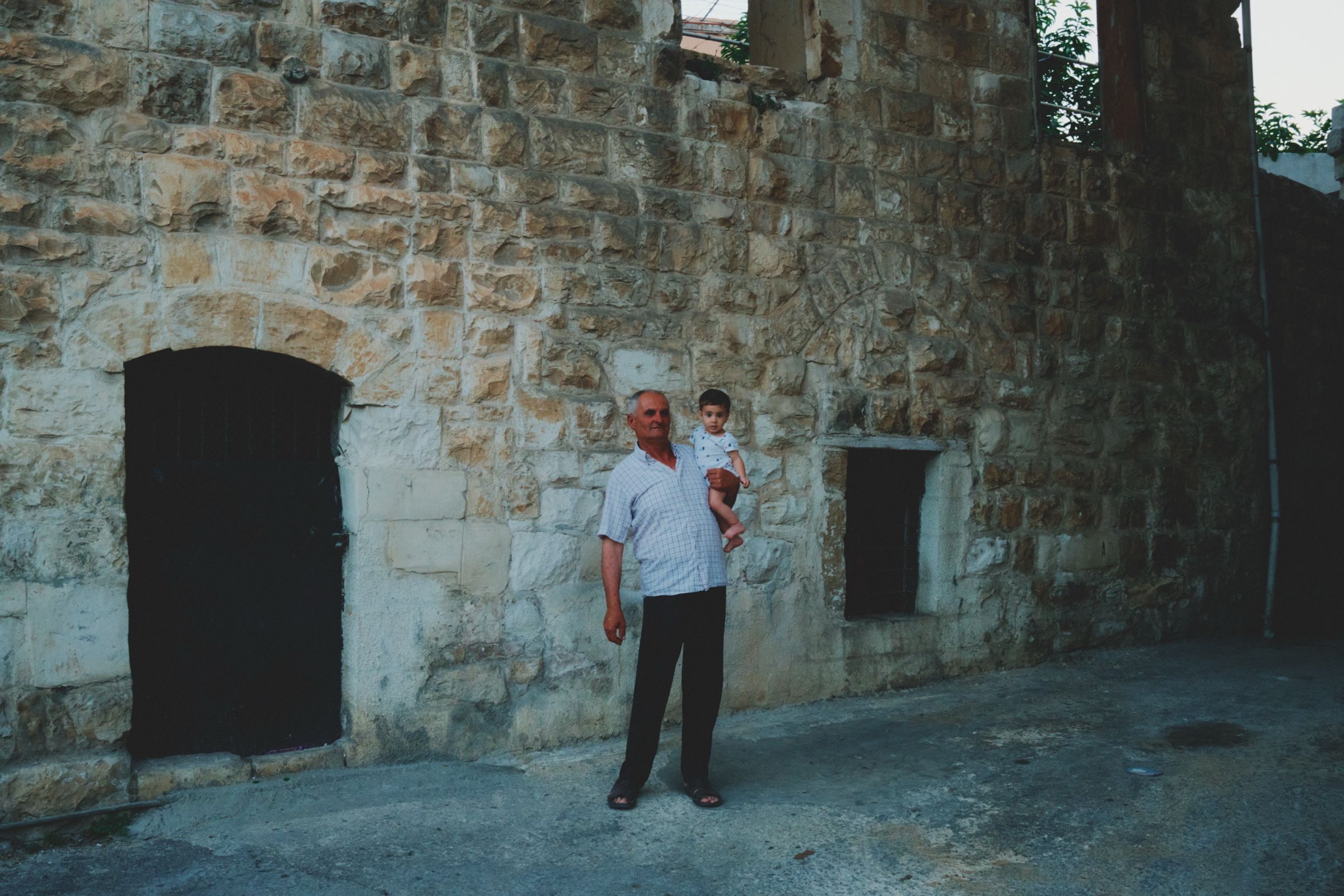 A grandfather holds his grandson near their home in one of the oldest village alleys.