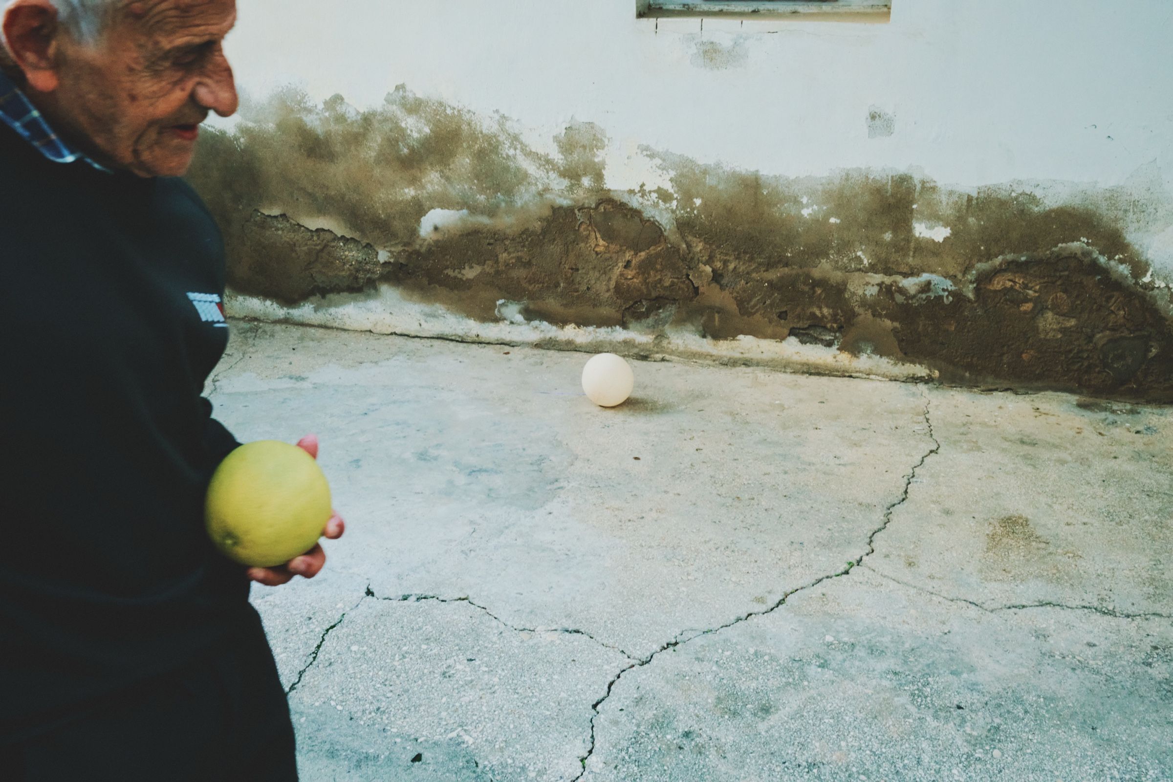 Salam, one of the oldest residents of the village, walks past the entrance of his house with cracked concrete and peeling walls, holding a grapefruit. The town of Joun, Lebanon, 2023.