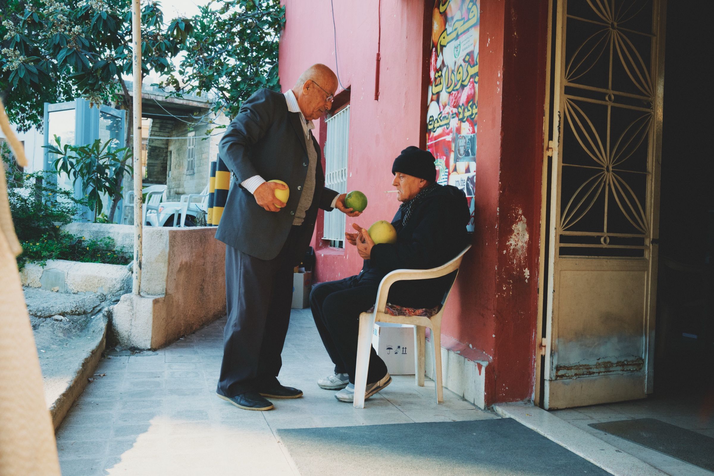 Two elderly men, one handing grapefruits to the other.